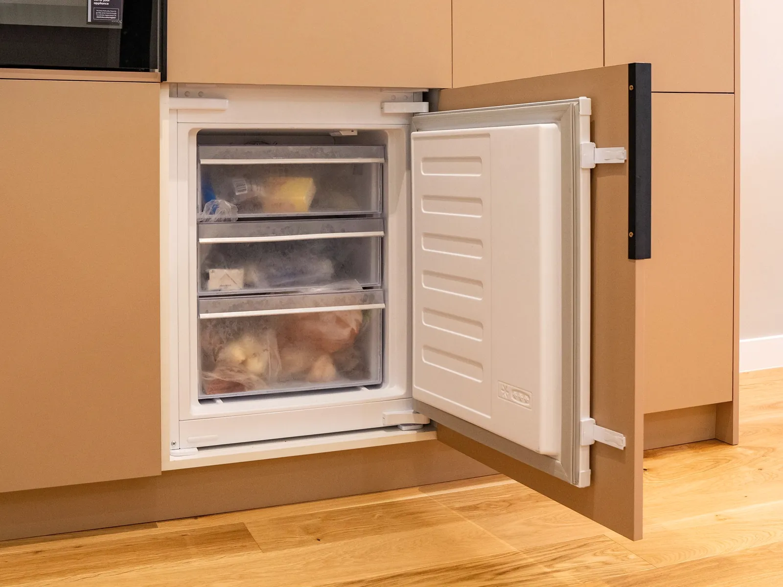 Built-in freezer with its door open and drawers of frozen food inside