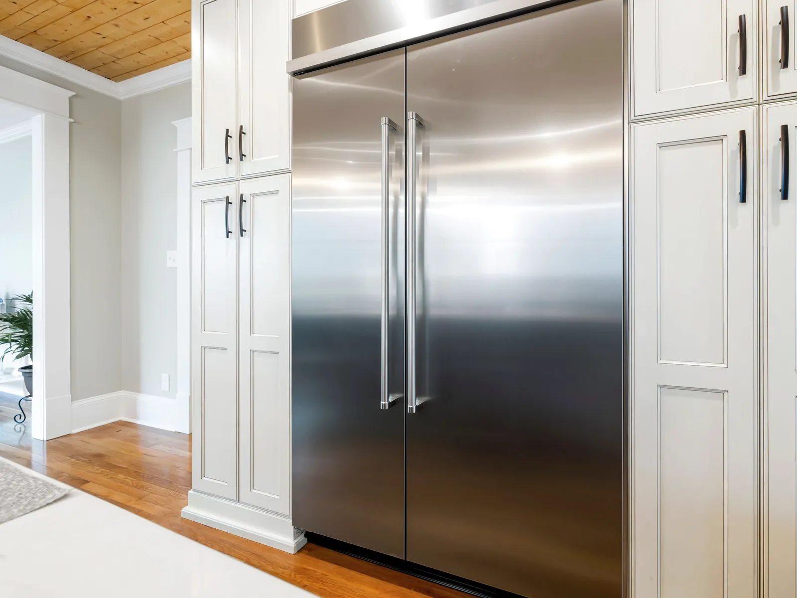 Stainless steel built-in refrigerator between white kitchen cabinets