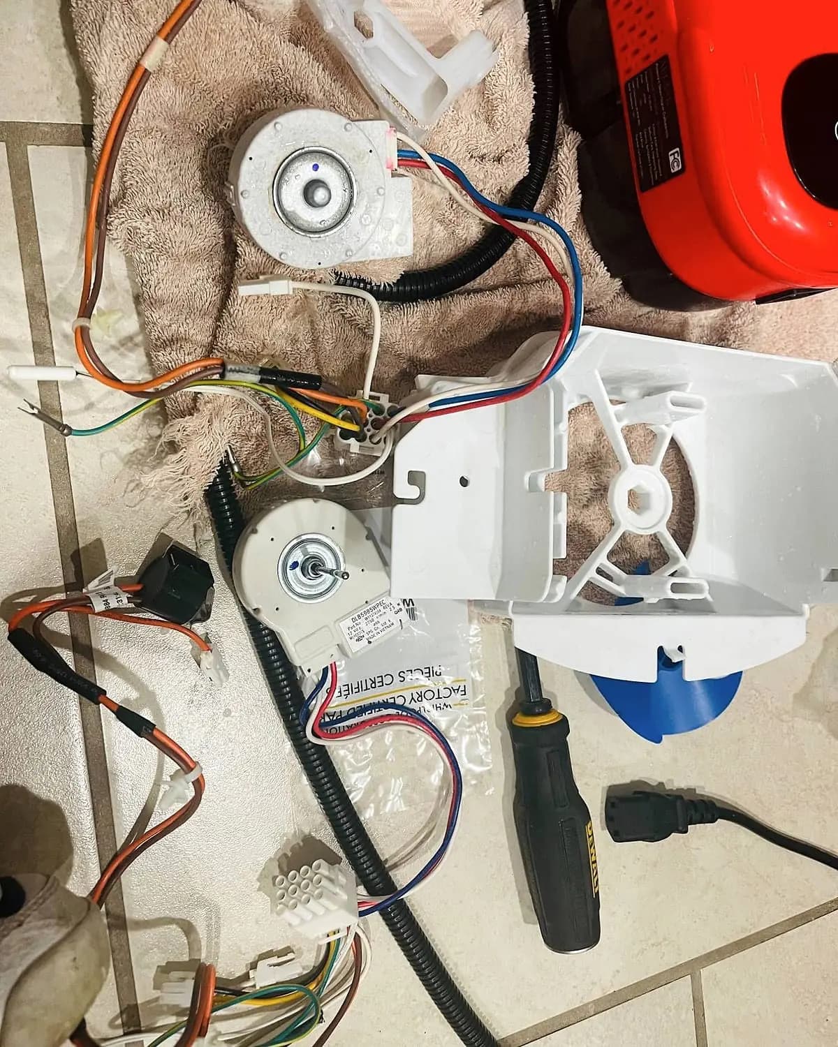 Refrigerator evaporator fan motors, wiring and fan housing laid out on a towel next to a screwdriver