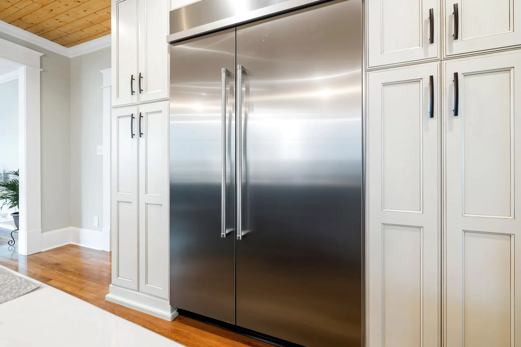Stainless steel built-in refrigerator in a bright kitchen with white cabinets
